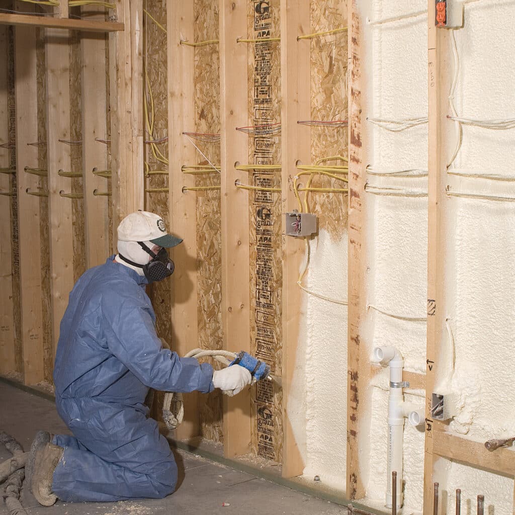 Technician installing spray foam in a wall while wearing a gas mask.
