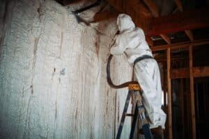 A worker doing spray foam insulation on the walls, covered in protective body gear